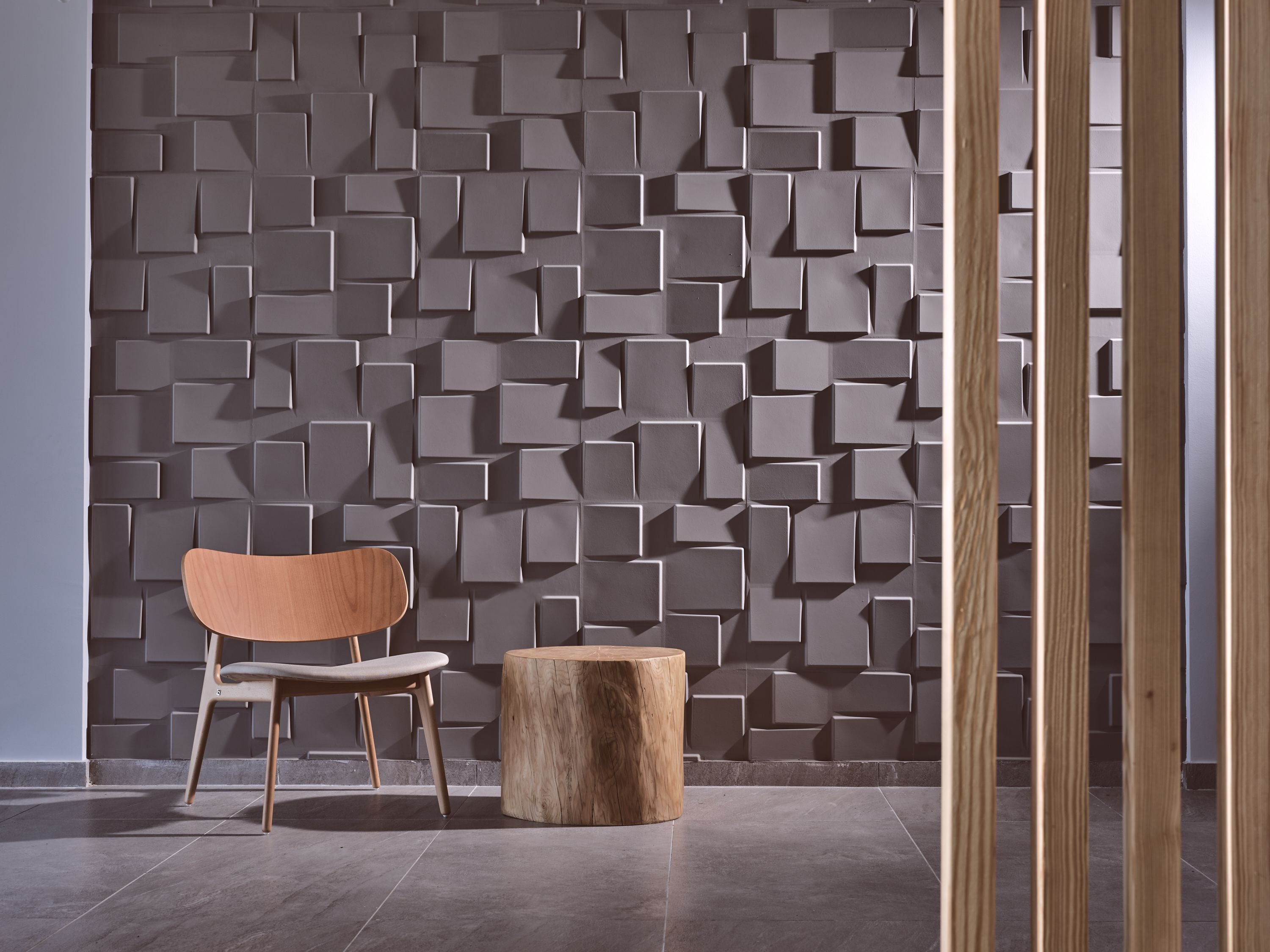 Een modern interieur met een geometrisch wandontwerp, een houten stoel en een rond houten krukje.