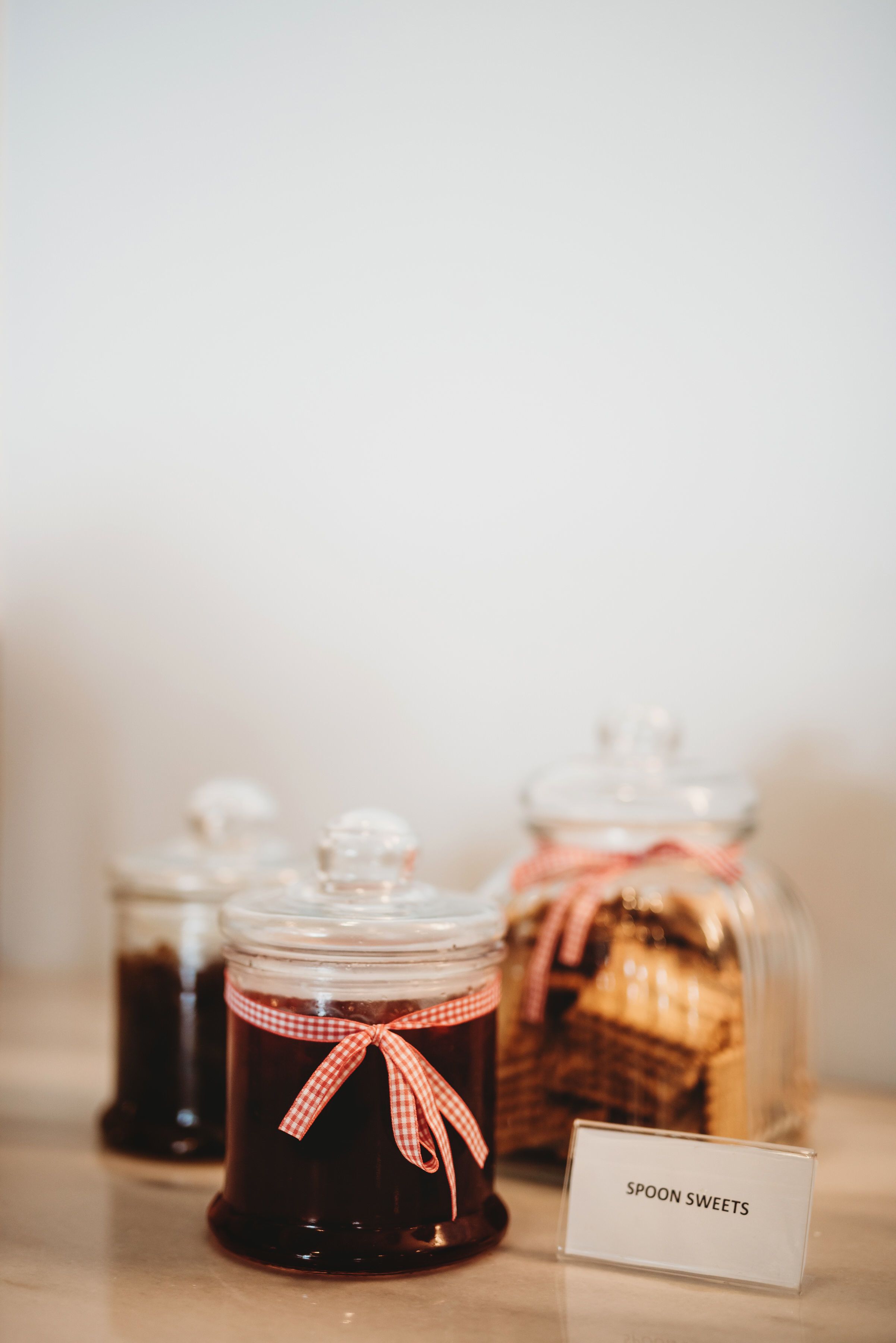 Three glass jars with labels, one labeled "Spoon Sweets," on a table.
