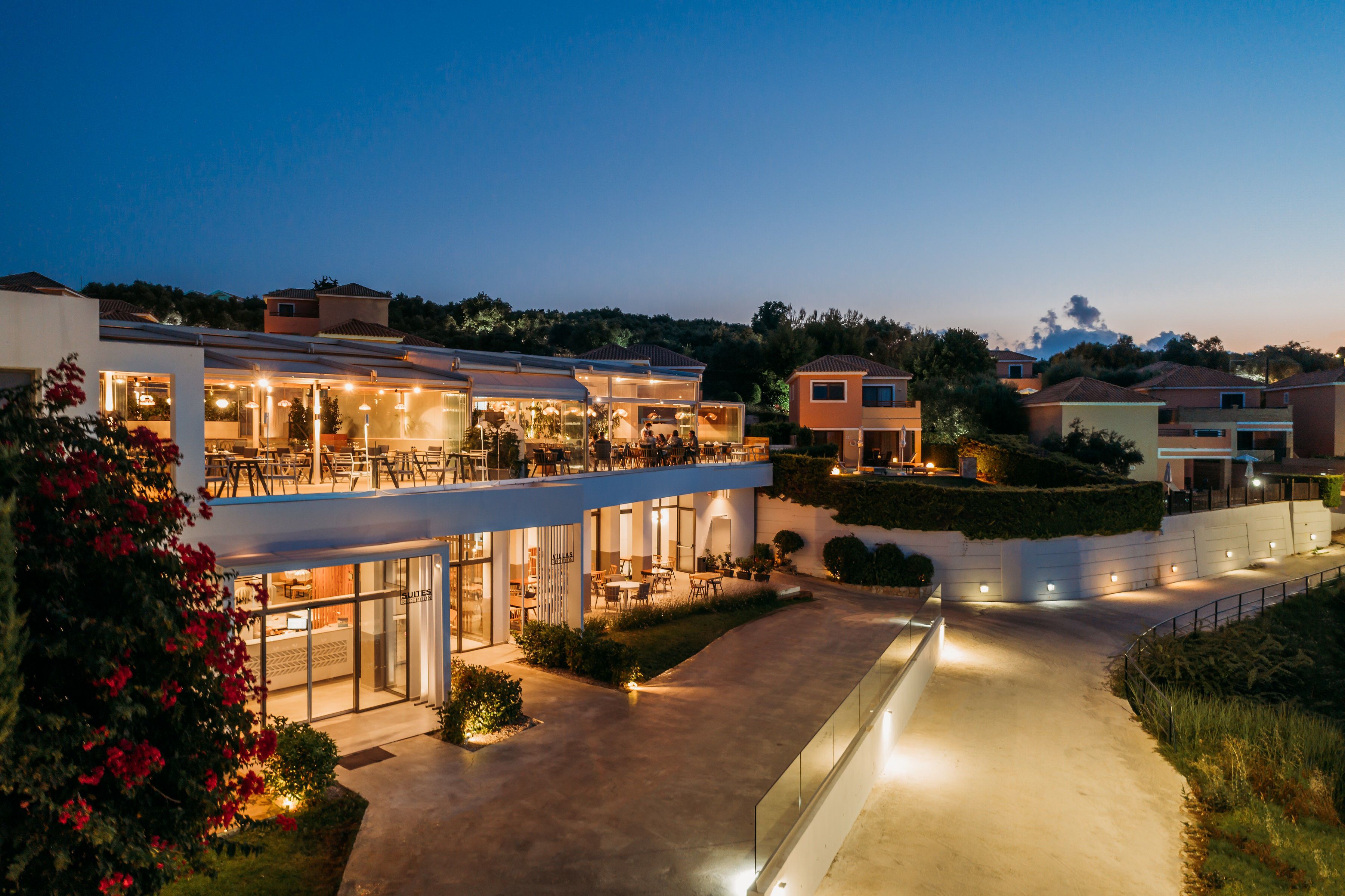 A modern hotel with multiple dining areas, outdoor seating, and a well-lit pathway.