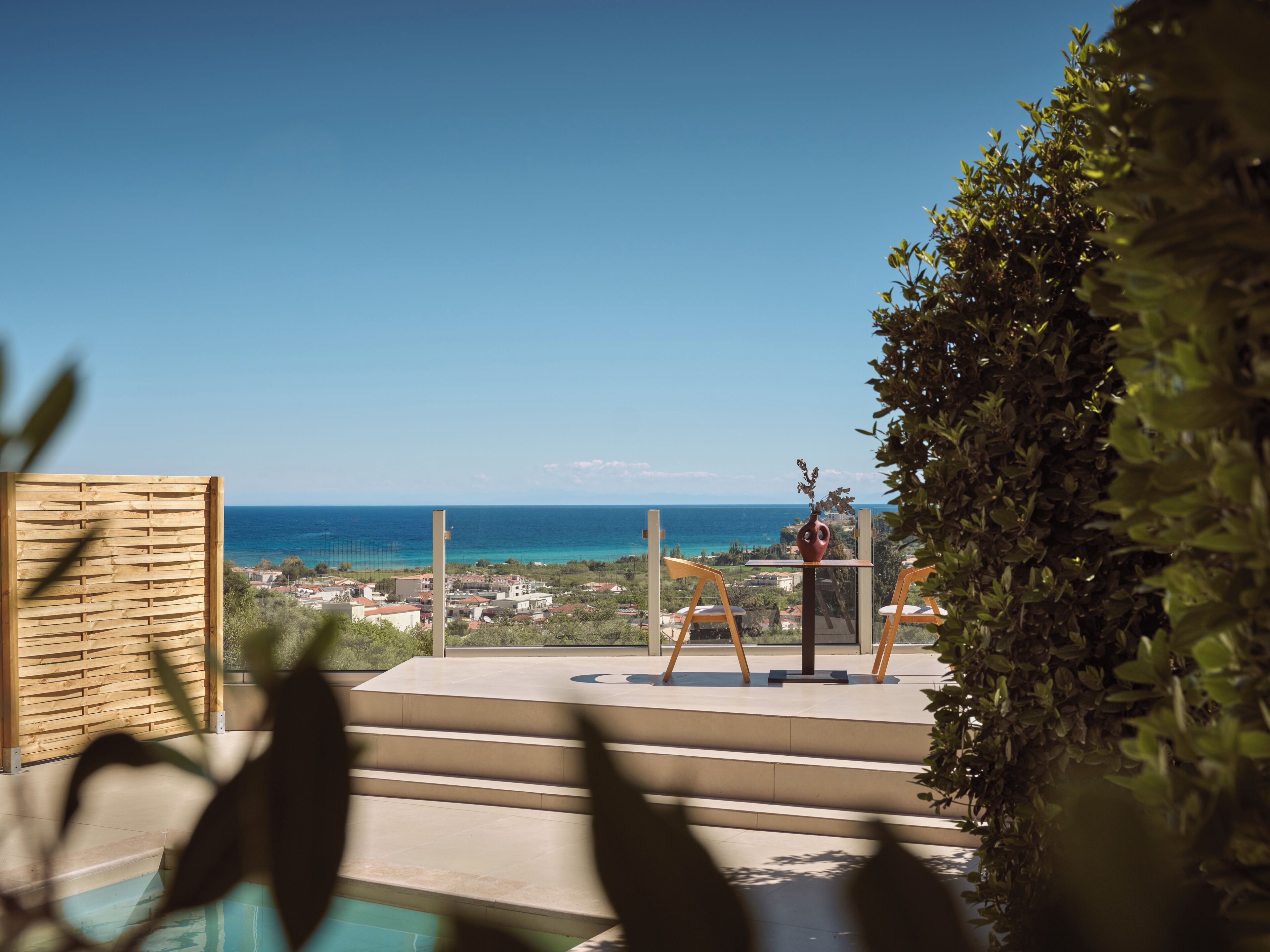 A terrace with a view of the sea, a wooden fence, and a table with chairs.