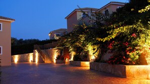 A paved courtyard with a staircase leading to a building, surrounded by flowering plants and illuminated by ambient lighting. - St. John Villas Zakynthos (Zakynthos)