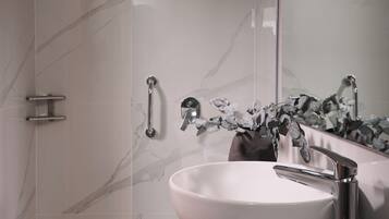 Un baño moderno con ducha de vidrio, lavamanos de mármol blanco y espejo con decoración floral.