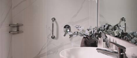 A modern bathroom with a glass-enclosed shower, a white marble sink, and a mirror with a floral decoration.