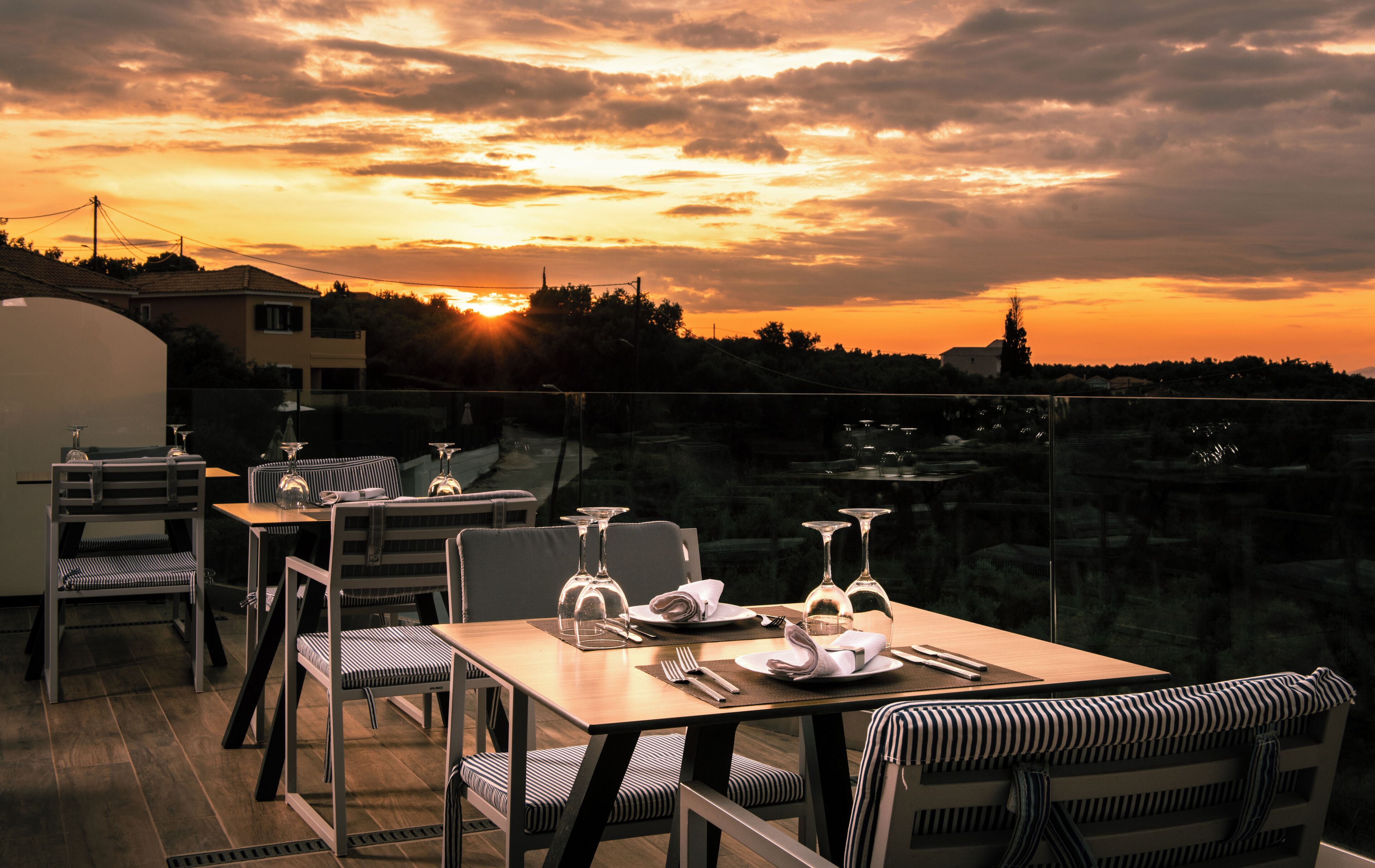 Zona pranzo all'aperto con tavoli e sedie, affacciata su una vista al tramonto.