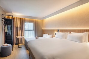 A hotel room with a large bed, a wardrobe, a small table, and a window with curtains.