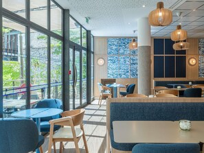 A modern restaurant interior with large windows, wooden furniture, and hanging pendant lights. - Novotel Marseille Centre Gare (Marseille)