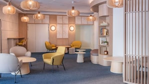 A modern lounge area with round tables, yellow chairs, and wooden shelving with books.