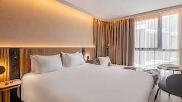 A hotel room with a large bed, bedside tables, a small table, and a chair.