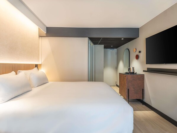 A modern hotel room with a large bed, a flat-screen TV, a wooden dresser, and a mirror.
