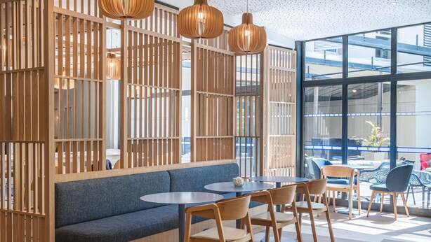 A modern interior with a wooden partition, a blue sofa, round tables, and chairs.
