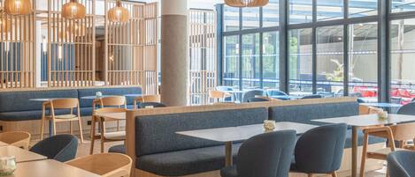 Un interior de restaurante moderno con mobiliario de madera, ventanas amplias y lámparas colgantes.