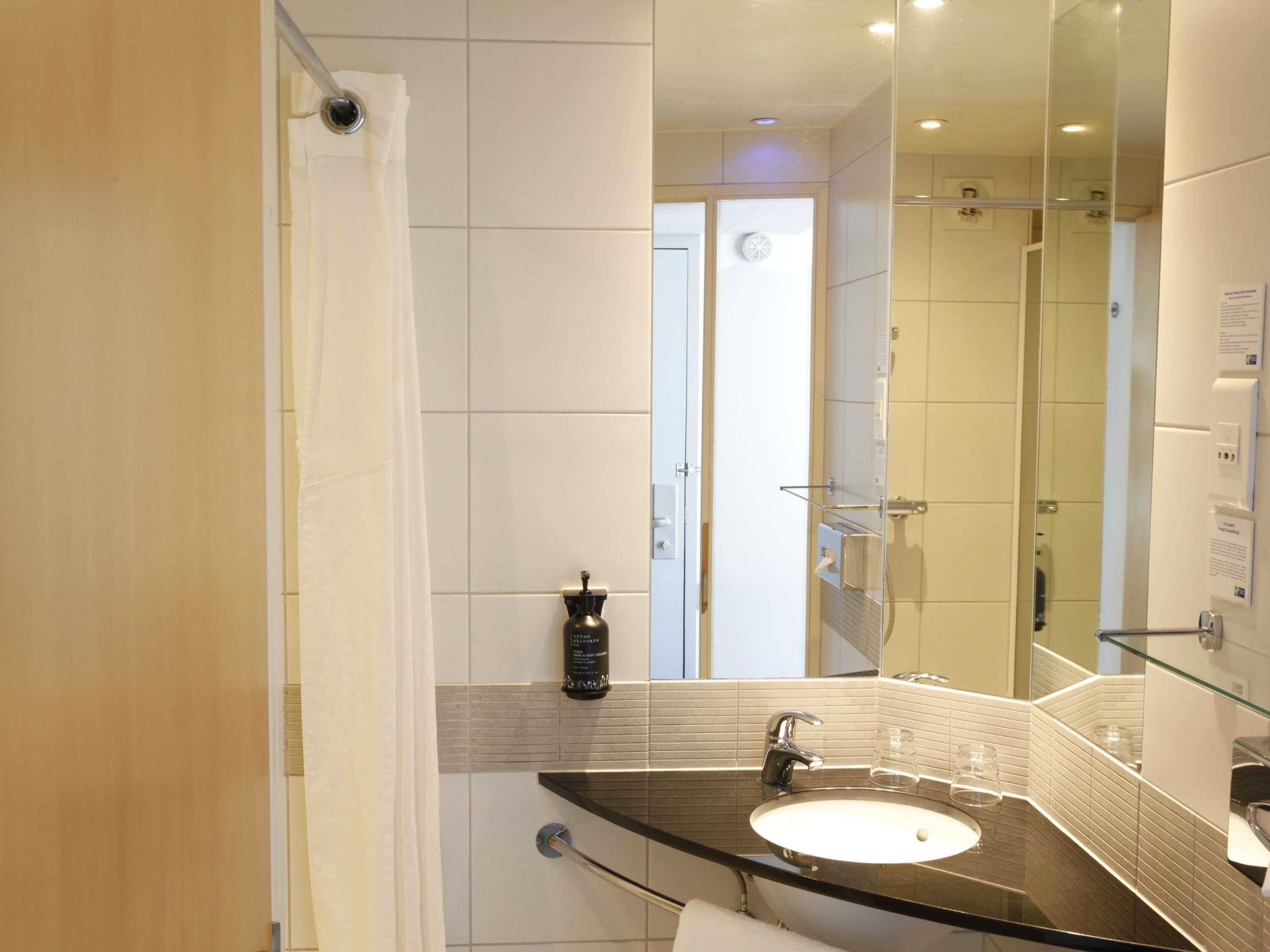 Une salle de bain moderne dotée d’une douche à parois de verre, d’un lavabo avec un plateau en verre et d’un miroir avec éclairage intégré.