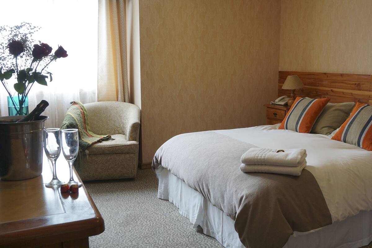 A hotel room with a bed, bedside table, chair, and a window with curtains.