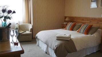 Habitación de hotel con cama, mesita de noche, silla y ventana con cortinas.