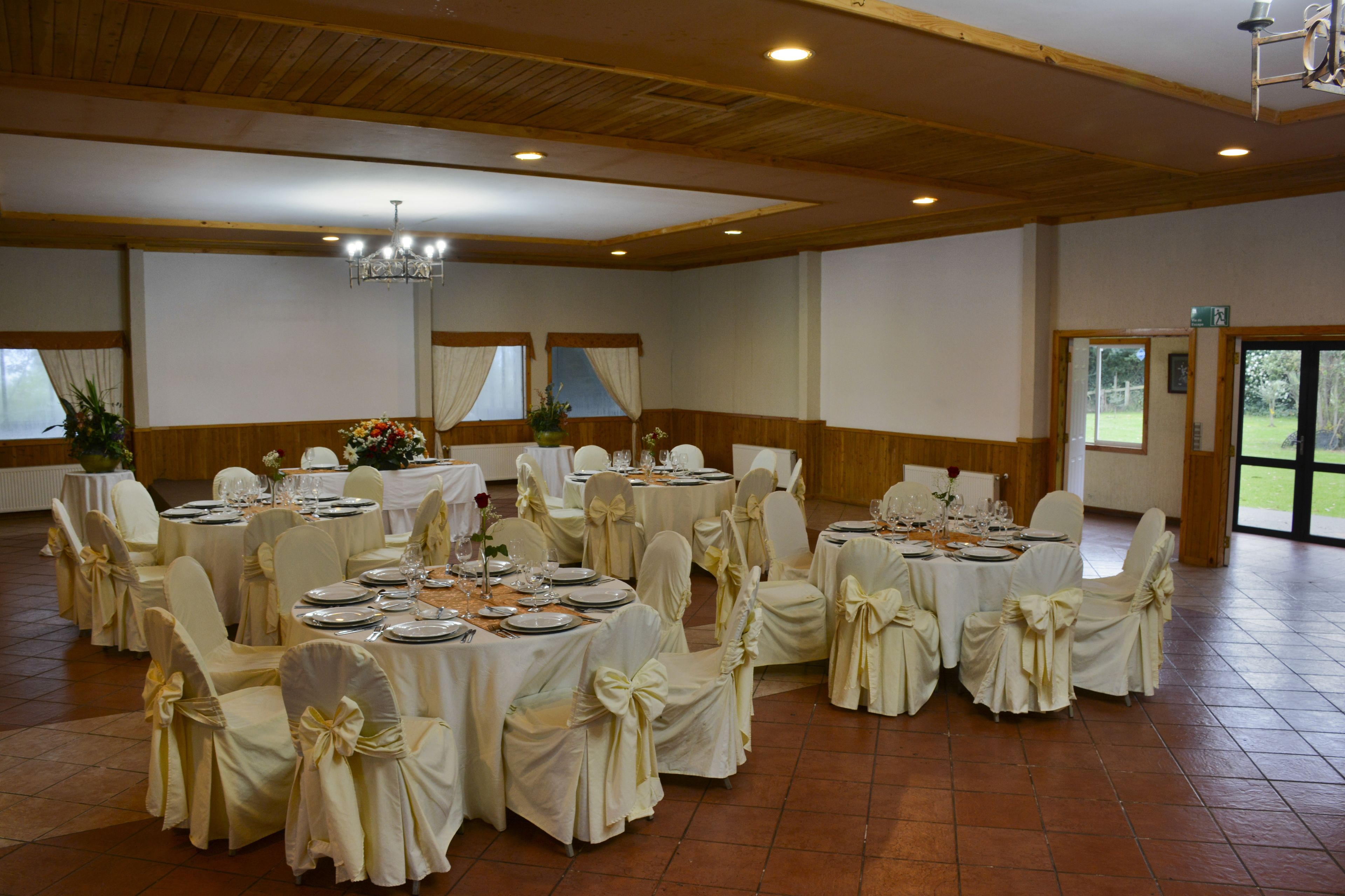 A banquet hall with round tables set for dining, each with white tablecloths and chairs adorned with bows.