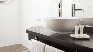 A modern bathroom with a large white sink, a mirror, and two toiletries on the counter.