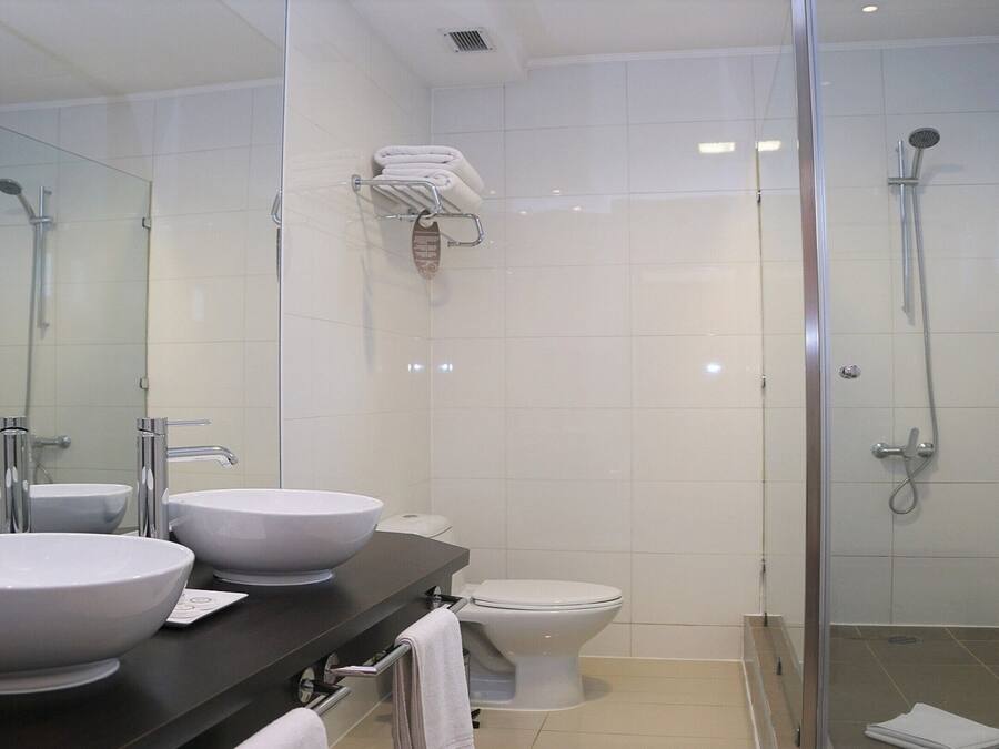 Un baño moderno con dos lavamanos, un inodoro y una zona de ducha con mampara de vidrio.