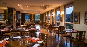 A restaurant with multiple dining tables, chairs, and large windows offering a view of the outdoors. - Solace Hotel Puerto Varas (Puerto Varas)