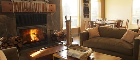 A cozy living room with a stone fireplace, a wooden coffee table, a sofa, and a dining area with chairs and a table.