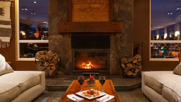 A cozy room with a stone fireplace, two sofas, a dining table with a meal, and a view of the city at night. - Solace Hotel Puerto Varas (Puerto Varas)
