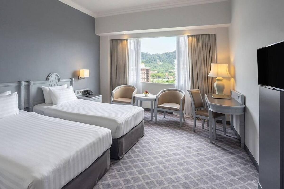 A hotel room with two beds, a small table, two chairs, a TV, and a window with curtains.