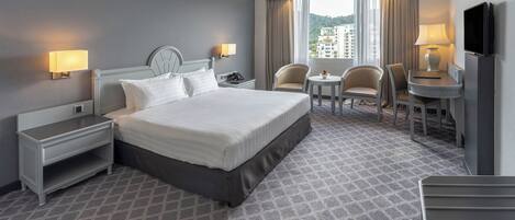 Habitación de hotel con una cama grande, mesitas de noche, un escritorio con silla, un televisor y una ventana con cortinas.