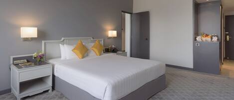 A hotel room with a large bed, two bedside tables with lamps, a nightstand, and a door leading to another room.