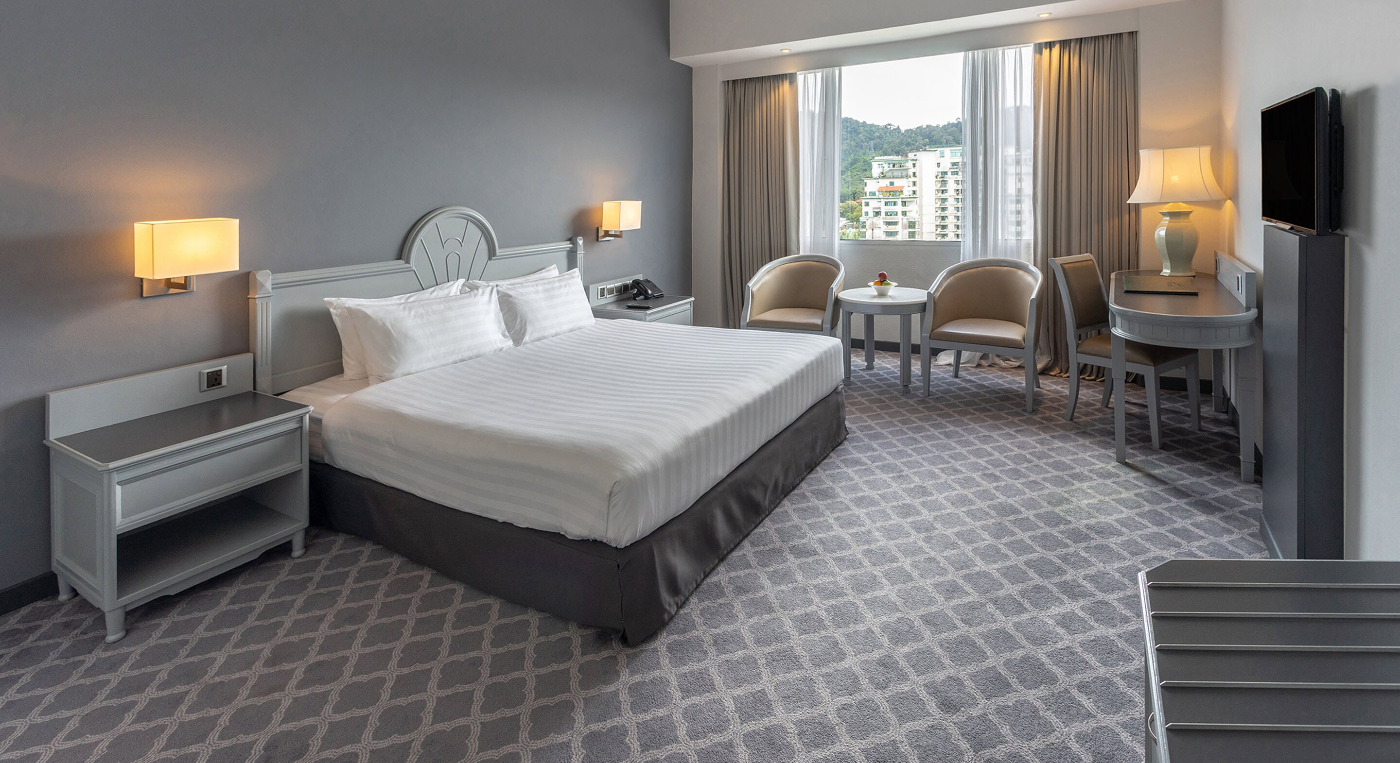 Une chambre d’hôtel avec un grand lit, deux tables de chevet, un bureau avec une chaise, une télévision et une fenêtre avec des rideaux.