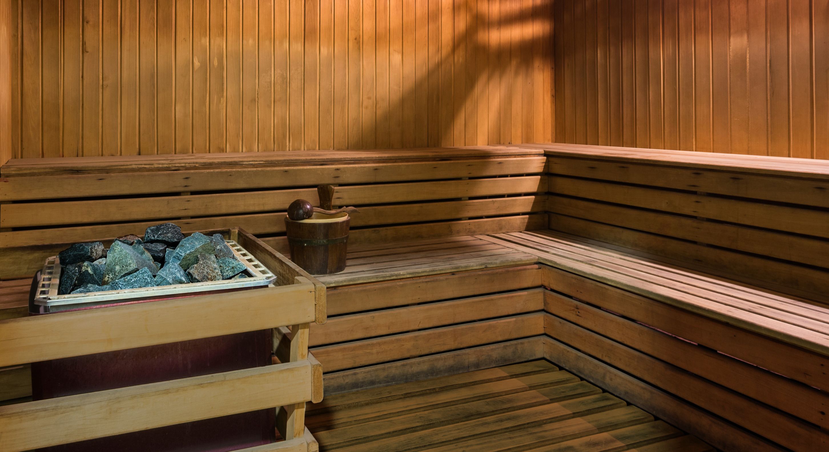 A wooden sauna with benches, a tray of stones, and a wooden bucket.