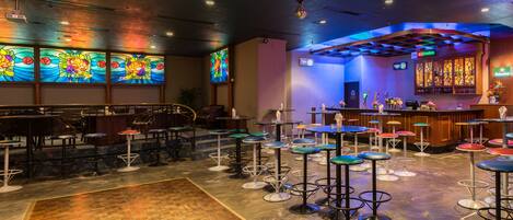 A bar area with multiple stools and tables, a bar counter with a sign, and colorful stained glass windows.