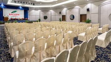 Een congrescentrum in Bayview Hotel Langkawi, Maleisië, met rijen stoelen bekleed met witte stof, een podium en een blauwe gordijnen achtergrond.