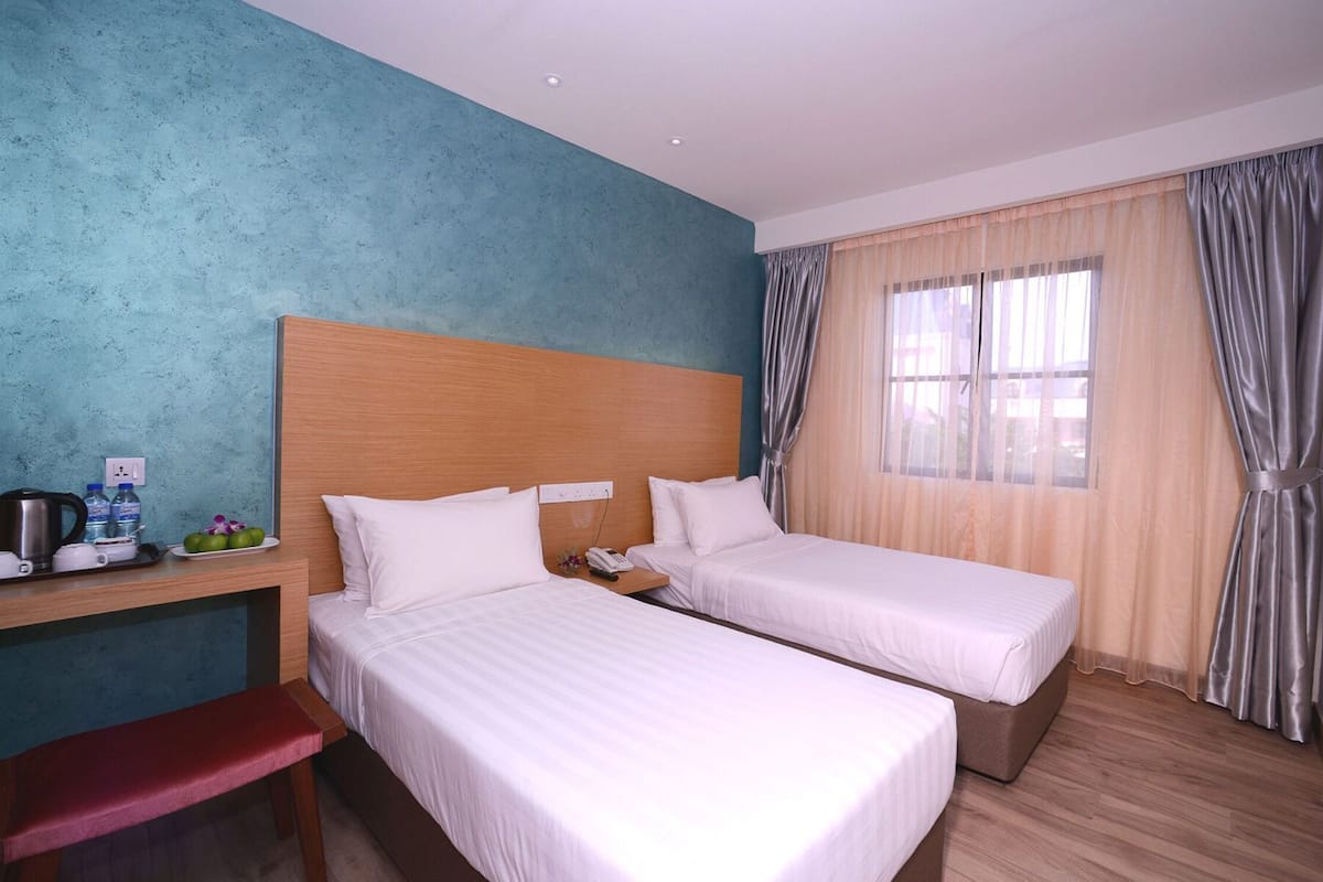 A hotel room with two beds, a desk with a kettle, water bottles, and a phone.