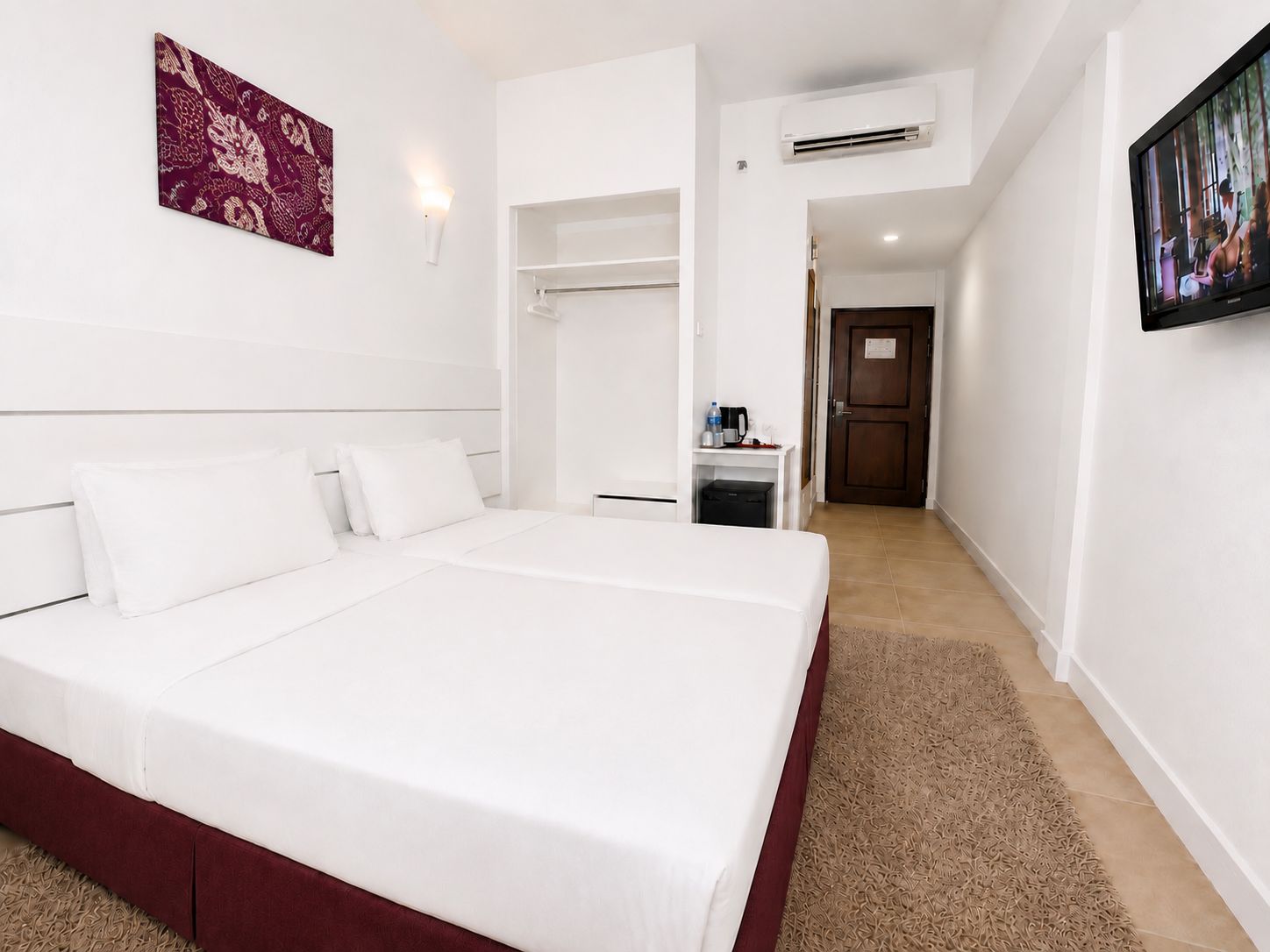 A hotel room with a large bed, a wardrobe, a desk with a chair, an air conditioning unit, and a television.