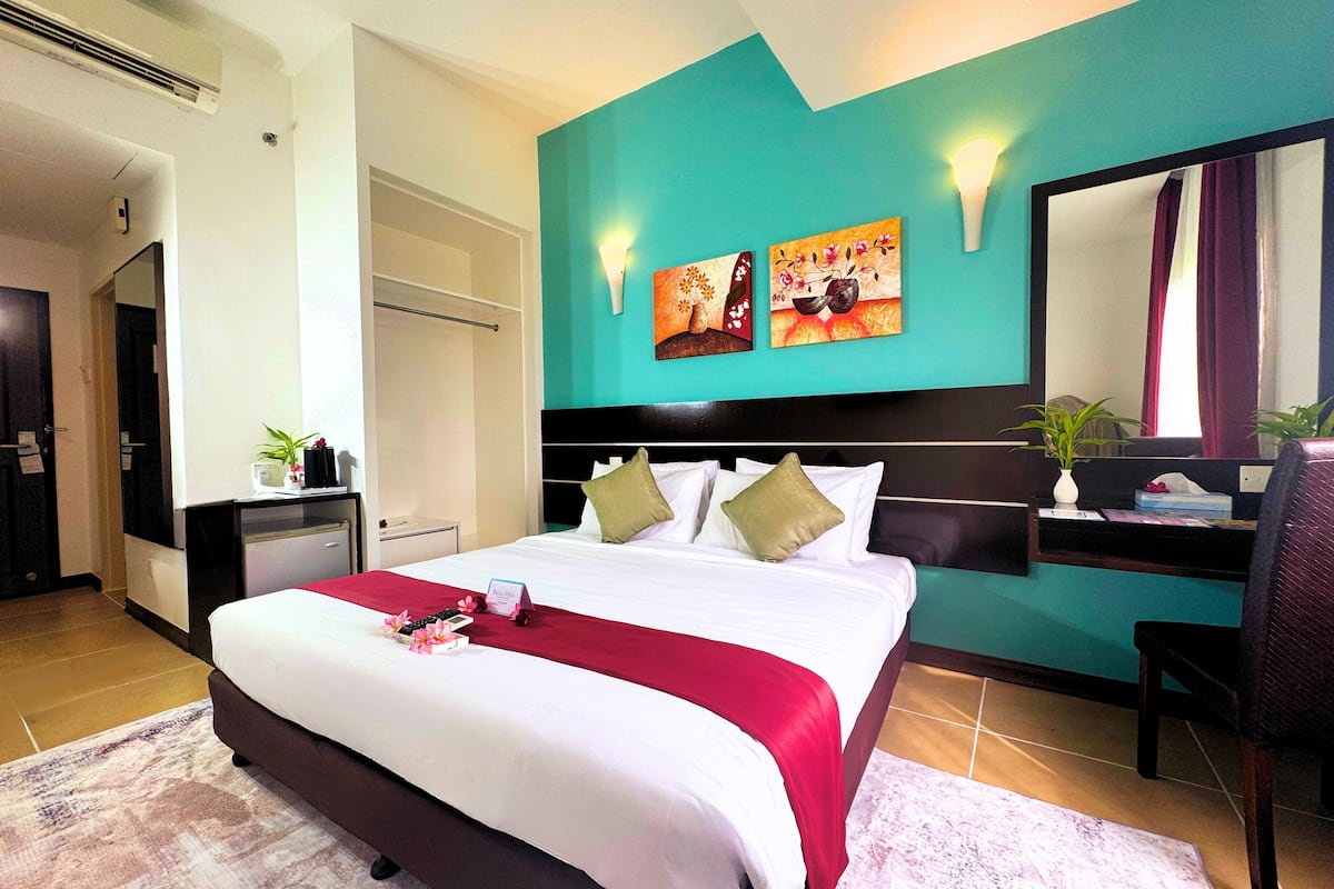 A hotel room with a bed, a desk, a chair, a mirror, and artwork on the wall.