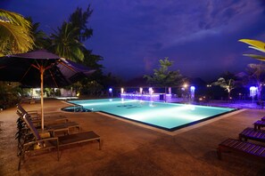 A nighttime swimming pool area with lounge chairs and umbrellas, surrounded by palm trees and illuminated by ambient lighting. - Bella Vista Waterfront Resort (Langkawi)
