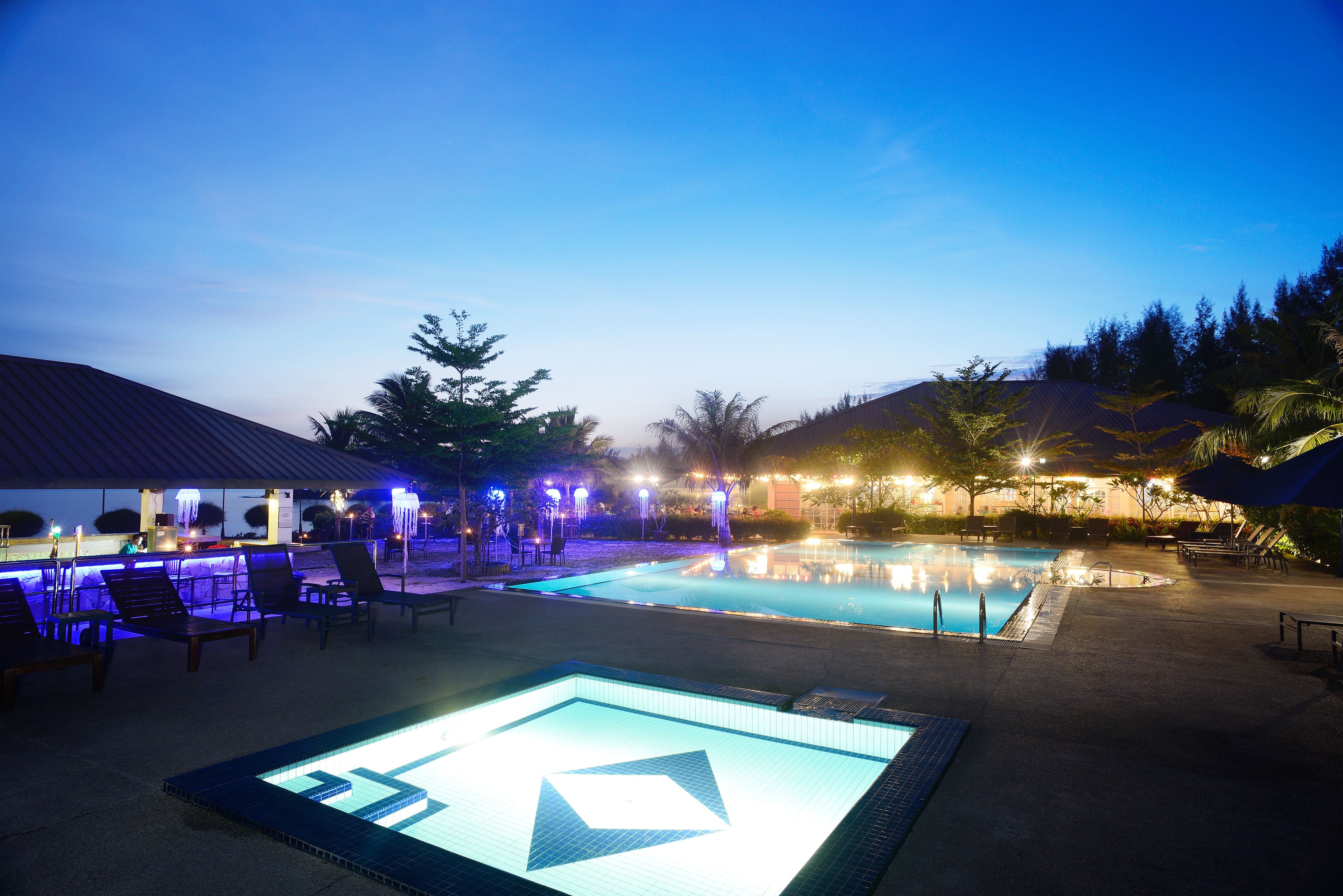 A pool area with lounge chairs and a water feature at dusk.