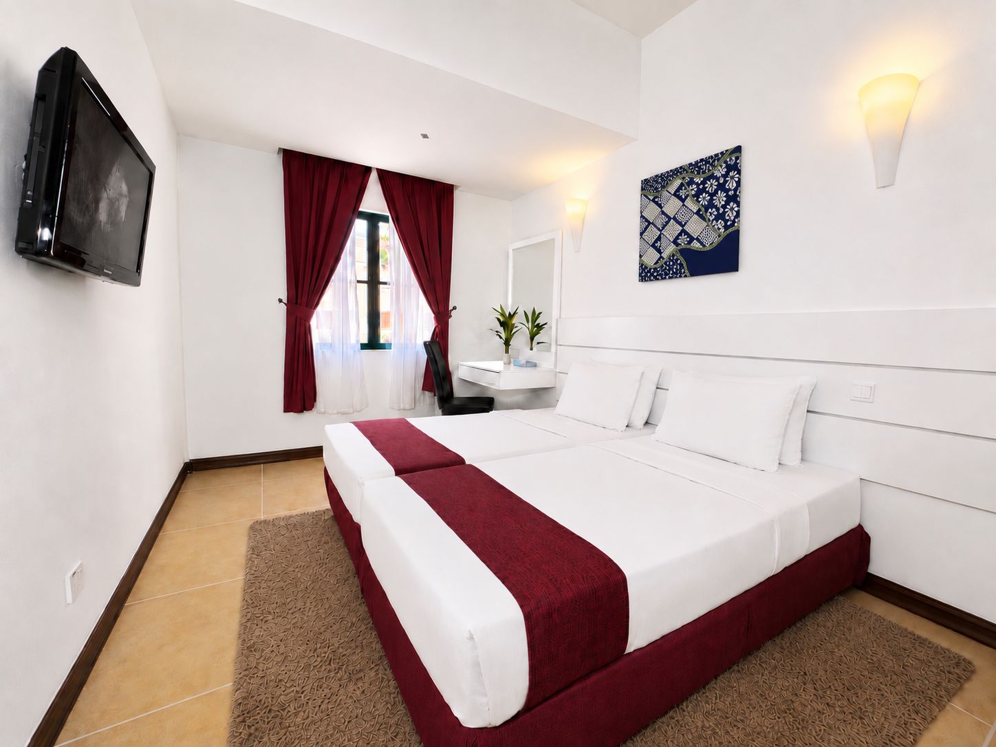 A hotel room with a bed, a desk, a chair, a TV, and a window with curtains.