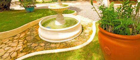 A fountain with two tiers, surrounded by a stone pathway and lush greenery.
