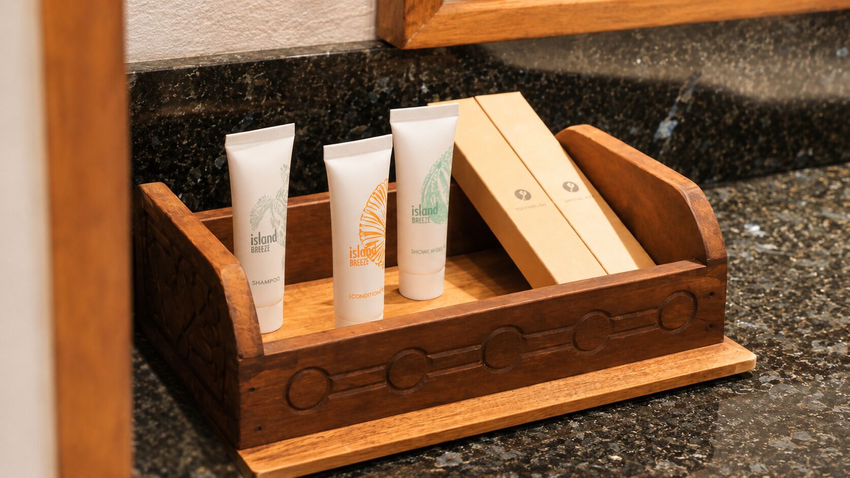 Una bandeja de madera con tres botellas de productos Island Breeze y una caja sobre una encimera de granito.