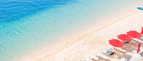 A beach with clear water, white sand, and red umbrellas.