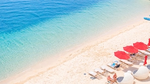 A beach with clear water, white sand, and red umbrellas.
