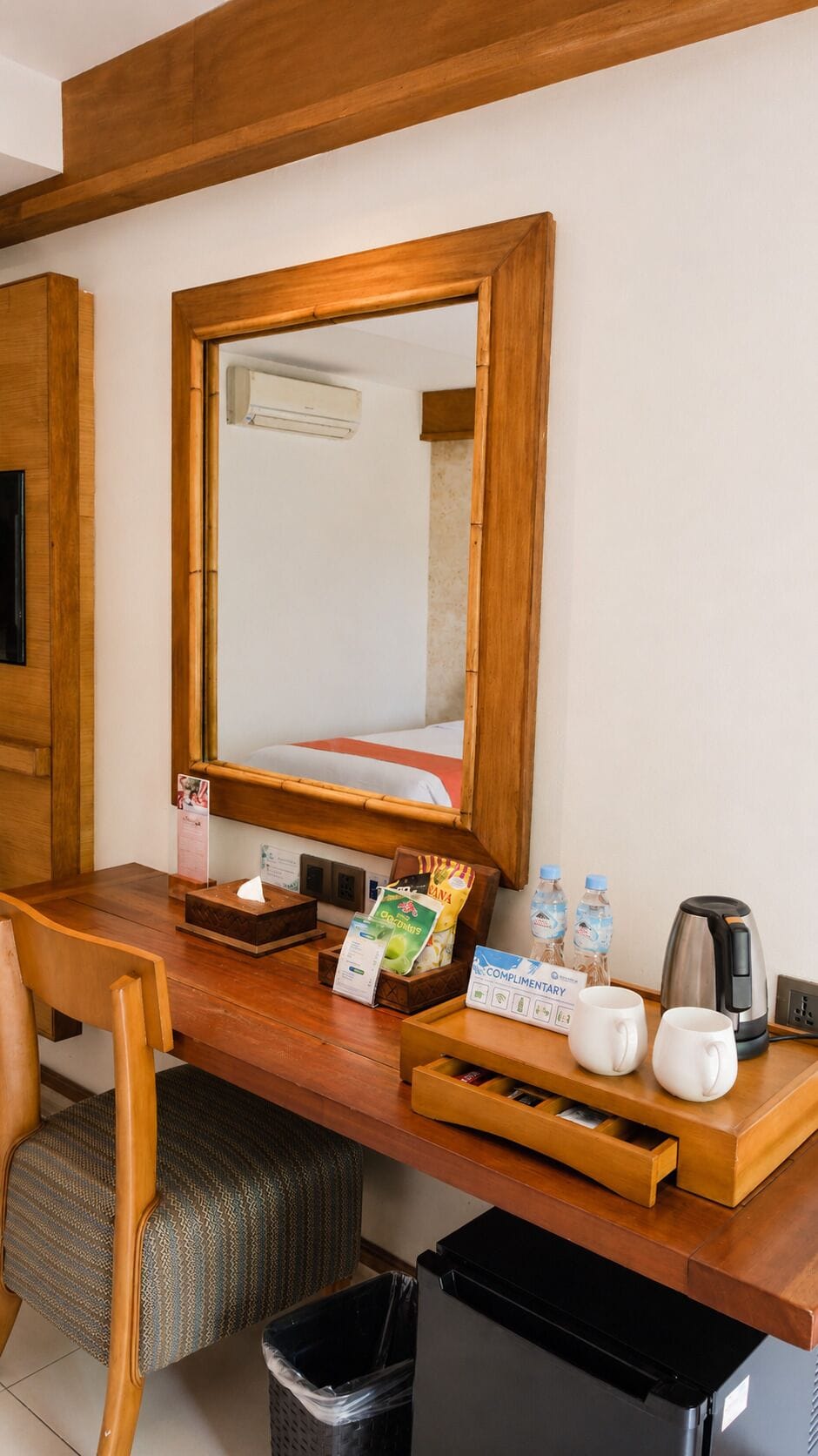 Ein Hotelzimmer mit Schreibtisch aus Holz, einem Spiegel, einem Mülleimer, einer Kaffeemaschine und einem Tablett mit Badaccessoires.