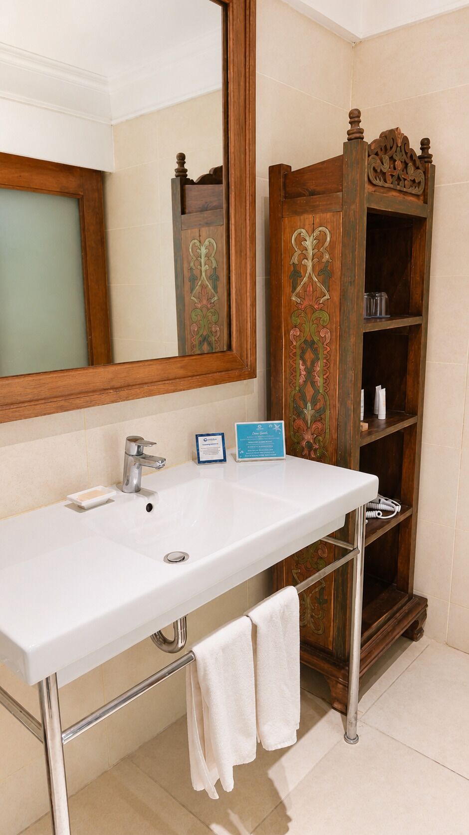 Une salle de bain avec un lavabo blanc, un miroir et un meuble-lavabo en bois doté d’étagères.