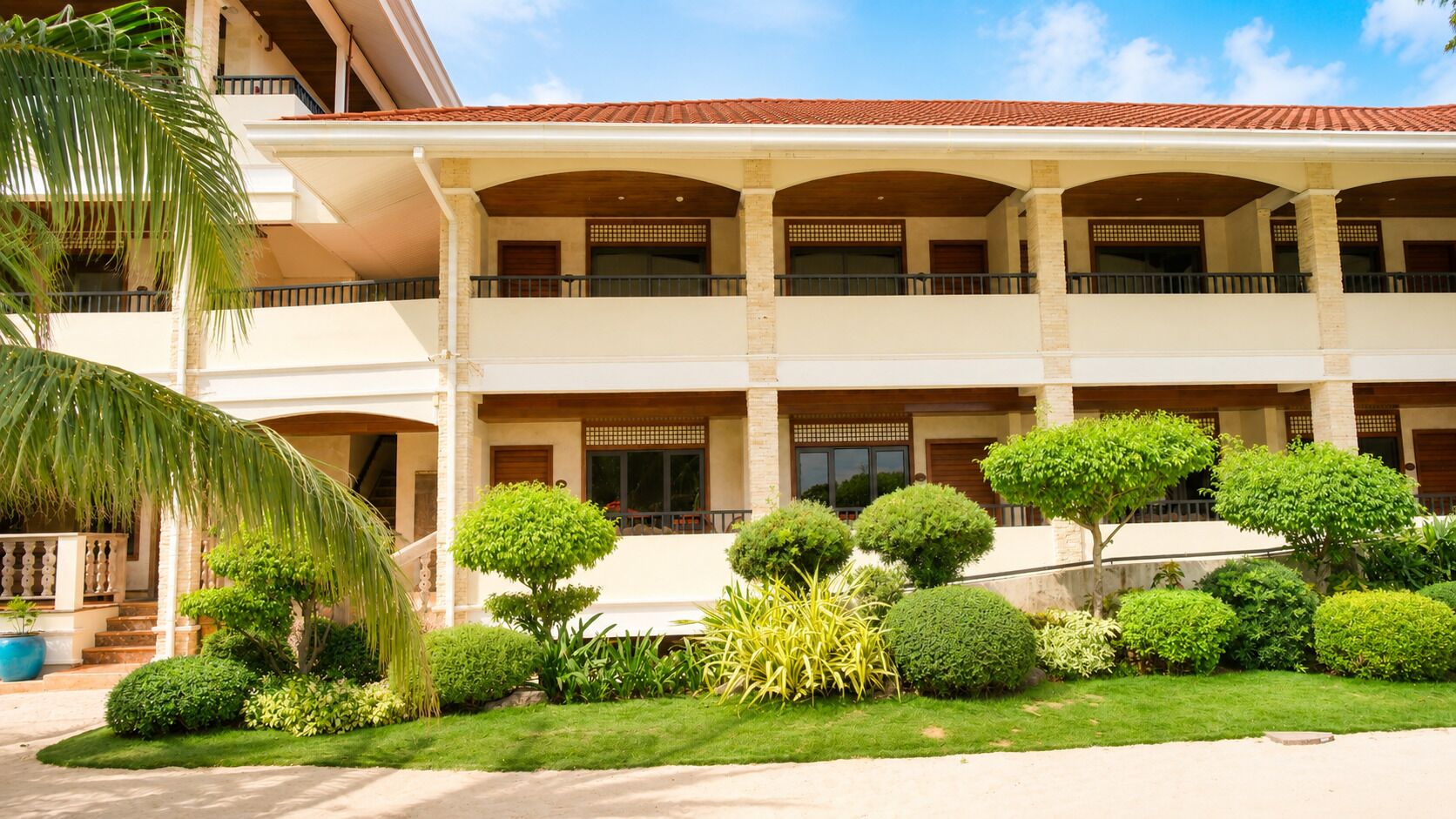 A multi-story building with a covered balcony area and a well-maintained garden with various shrubs and a palm tree.