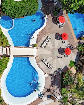 A large outdoor swimming pool with multiple lanes, surrounded by lounge areas with umbrellas, and a central seating area with tables and chairs.