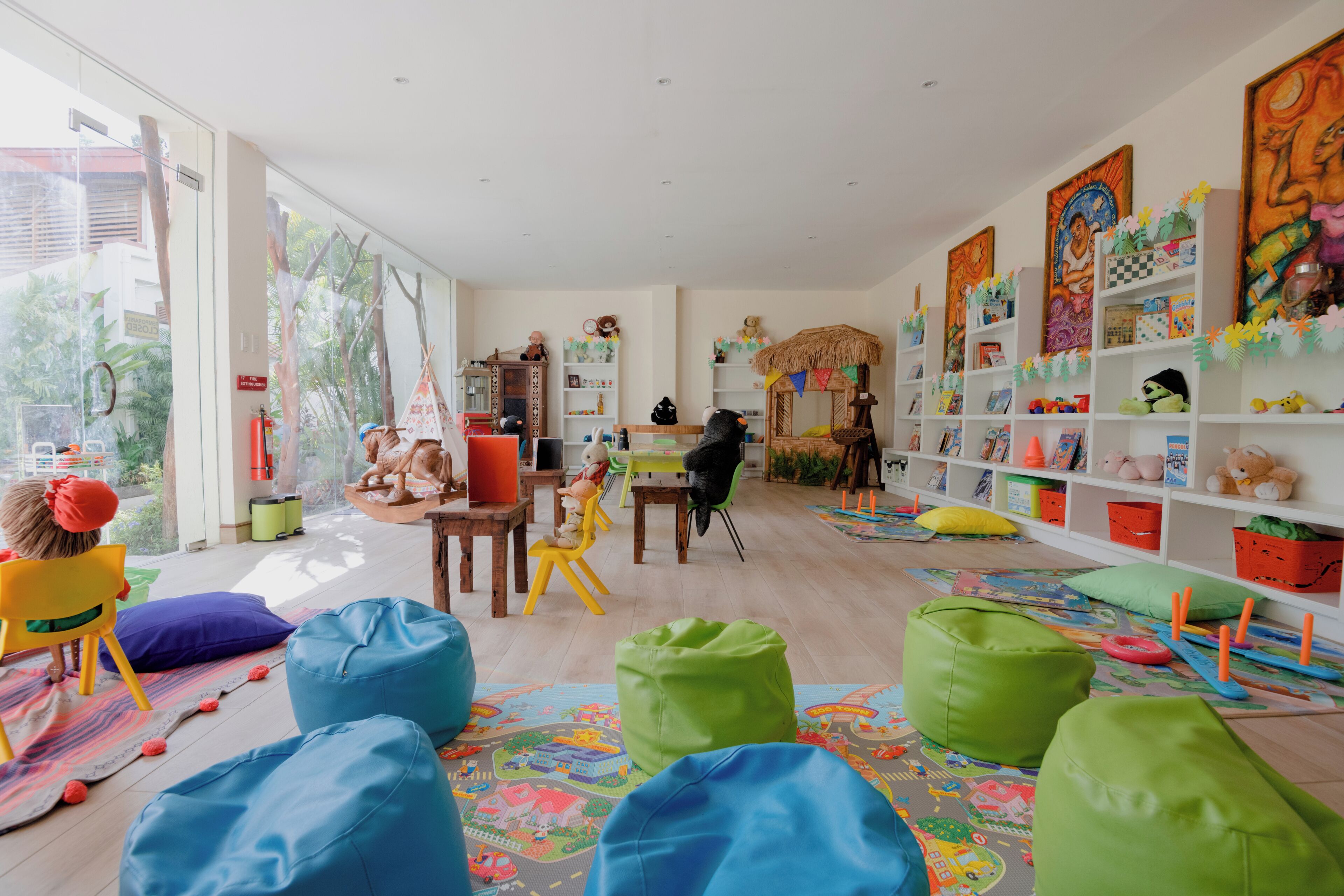 A spacious room with a large window, a play area with colorful bean bags, and a bookshelf filled with children's books and toys.