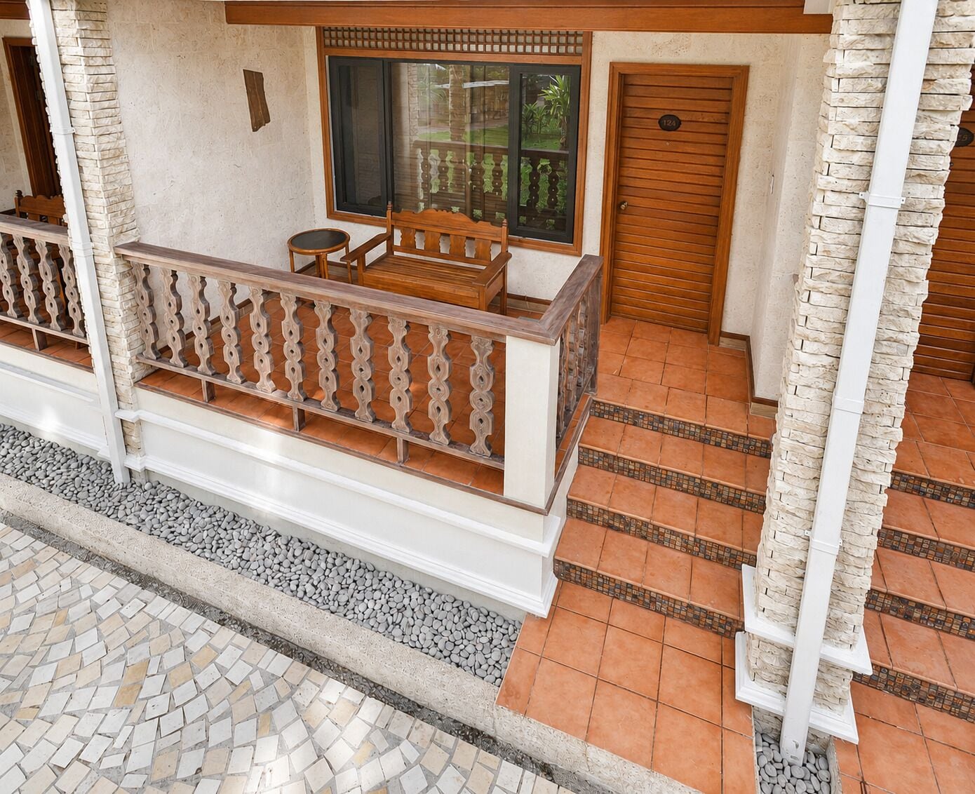 A balcony with a wooden bench, a window with a view, and a door with a number plate.