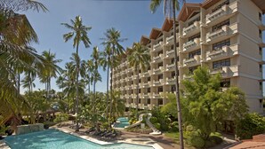 Un complexe hôtelier doté d’une piscine, de palmiers et d’un immeuble à plusieurs étages avec des balcons.