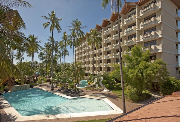 Un resort con piscina, palmeras y un edificio de varios pisos con balcones.