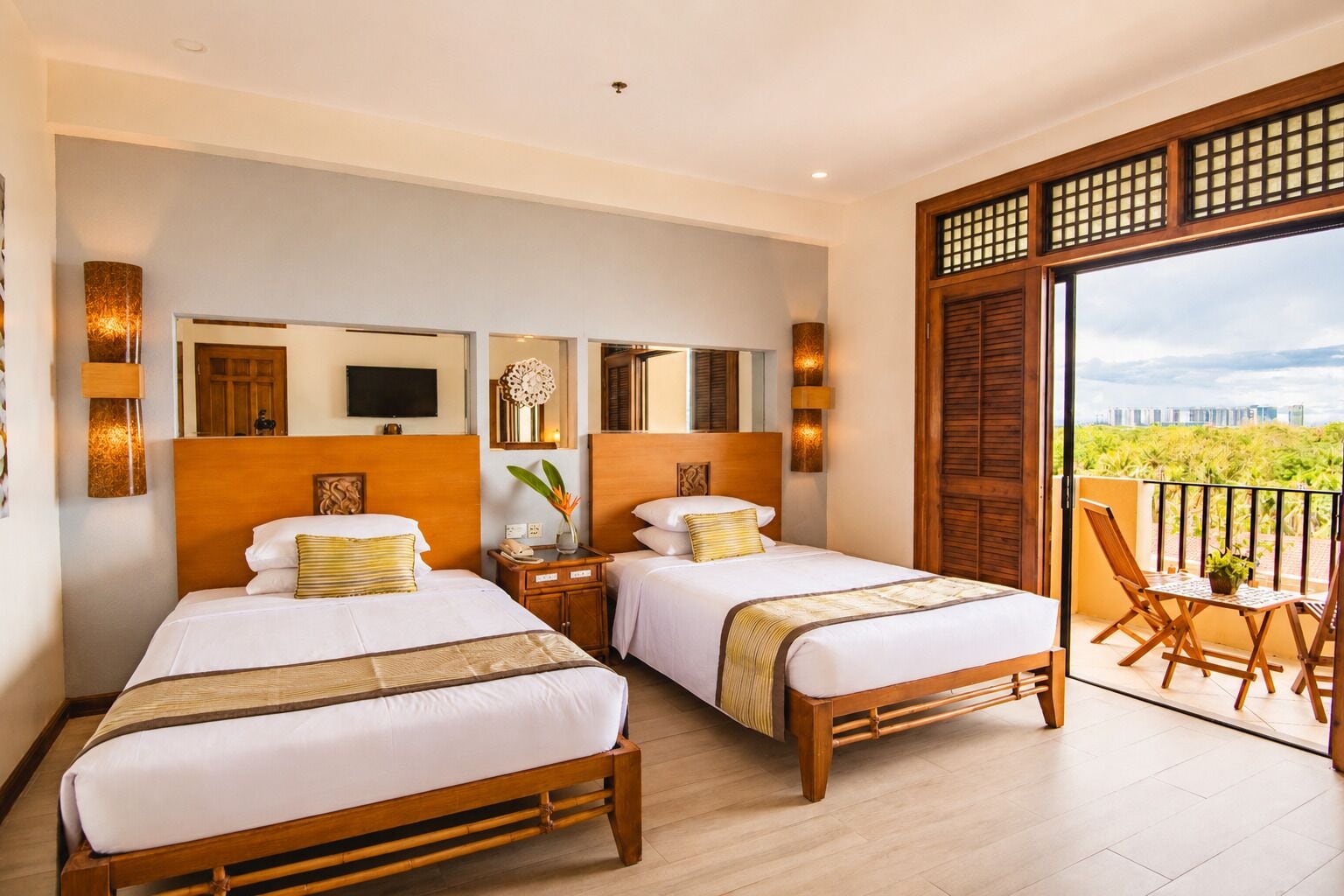 A hotel room with two beds, a TV, a balcony with a view, and a cityscape in the background.